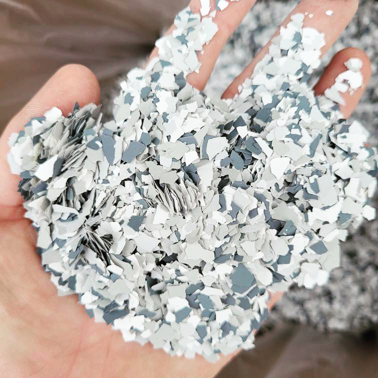 A person's hand is holding a cluster of small, irregularly shaped blue and white confetti pieces. The background is soft and indistinct.