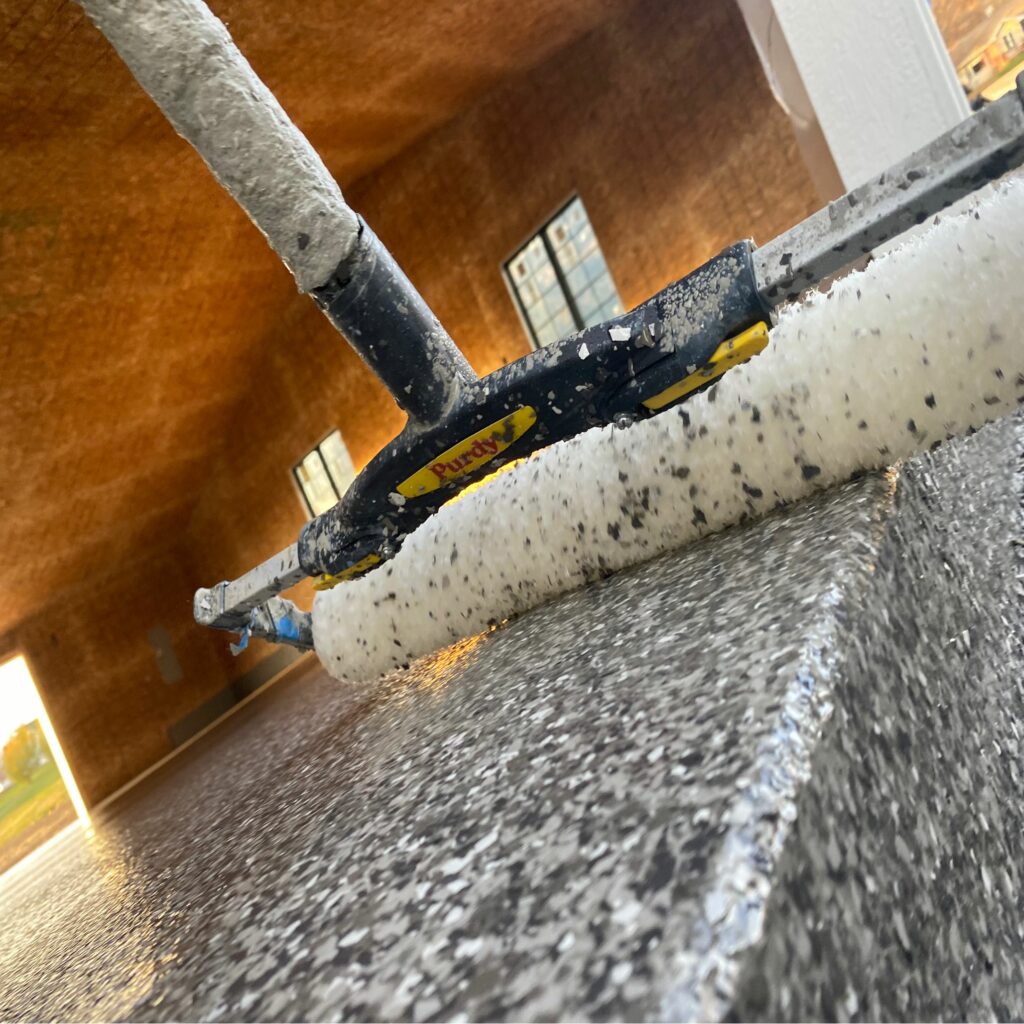 This is a close-up, low-angle photo showing a paint roller with yellow and black handles, resting on a textured surface, likely during a painting job.