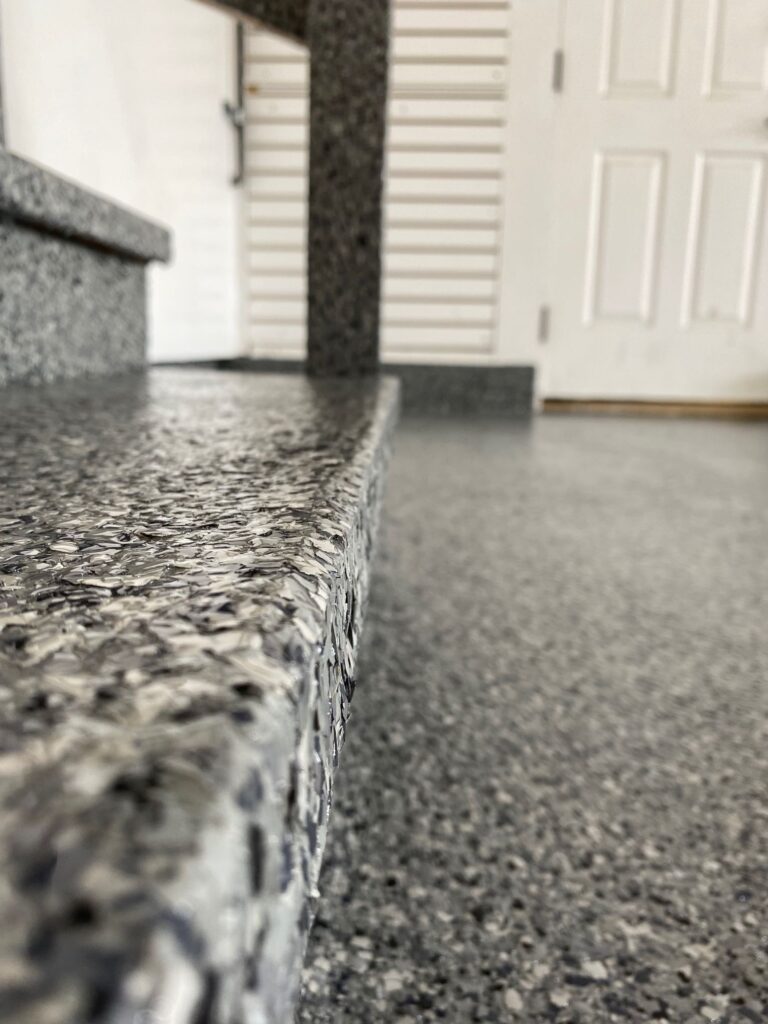 Close-up of a granite countertop edge with a speckled pattern, leading to a blurred background featuring a white door and a column.