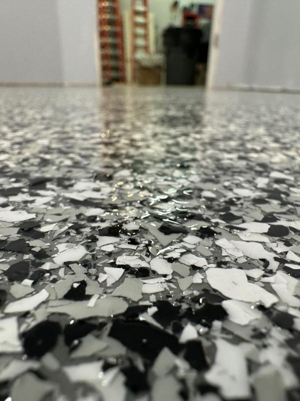 A close-up of a speckled floor, with scattered black and white fragments, glossy surface, leading towards an out-of-focus background with objects.