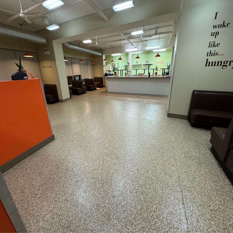 A spacious interior with speckled flooring, orange accent wall, seating areas, and a counter with hanging lights. A humorous quote about hunger adorns the wall.