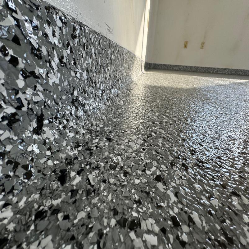 This image shows a shiny, speckled epoxy floor with metallic flakes transitioning up a wall, reflecting light, and creating a textured, glossy surface.